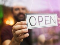 a man hangs an open sign at a store