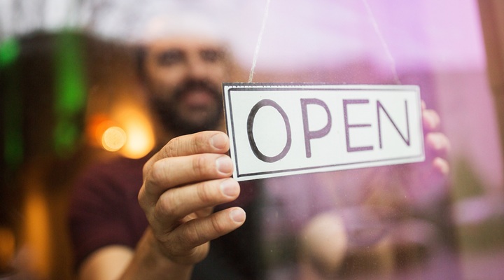 a man hangs an open sign at a store