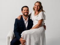 Woman in white dress sits on lap of man in black suit.