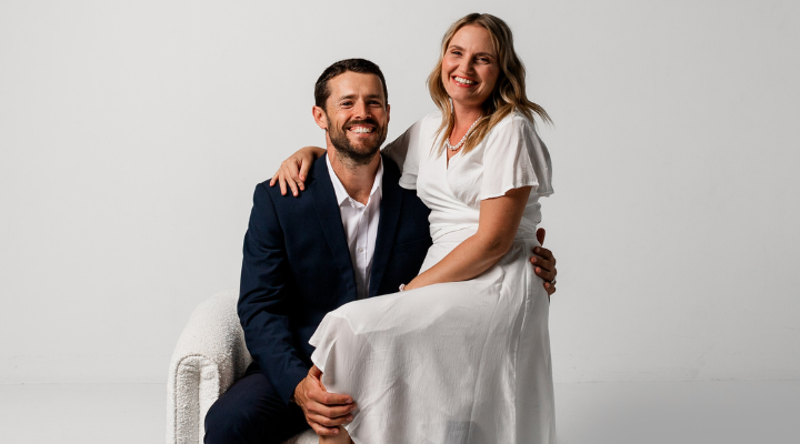 Woman in white dress sits on lap of man in black suit.