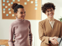 Business owner shakes hand of unknown in office with colleague looking on.