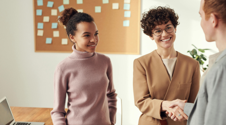Business owner shakes hand of unknown in office with colleague looking on.