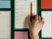 Table flat-lay of notebooks and hand holding pencil.