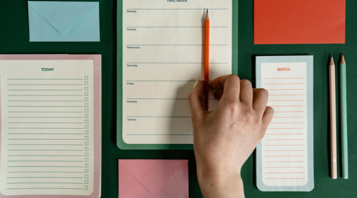 Table flat-lay of notebooks and hand holding pencil.