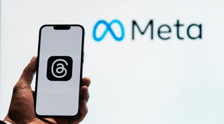 Hand holding up phone with Threads app on screen and Meta logo in the background