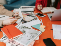 People working around an orange table with a stack of magazines.