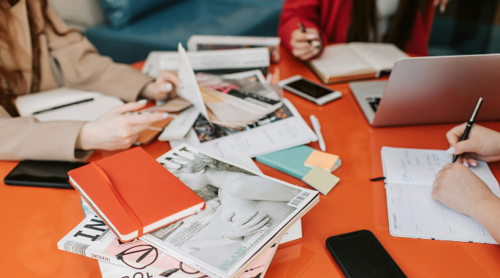 People working around an orange table with a stack of magazines.