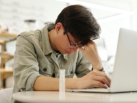 Man rubbing forehead while working at laptop.