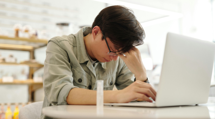 Man rubbing forehead while working at laptop.