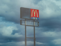 A McDonalds sign in front of a grey moody sky.