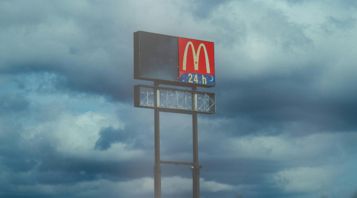 A McDonalds sign in front of a grey moody sky.