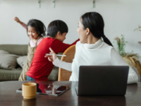 Mum sitting in front of laptop scolding kids playing behind her