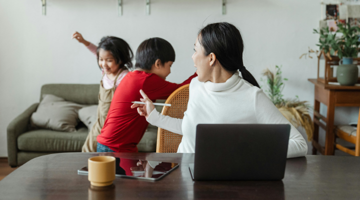 Mum sitting in front of laptop scolding kids playing behind her