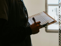 Person holding a clipboard by a shelf