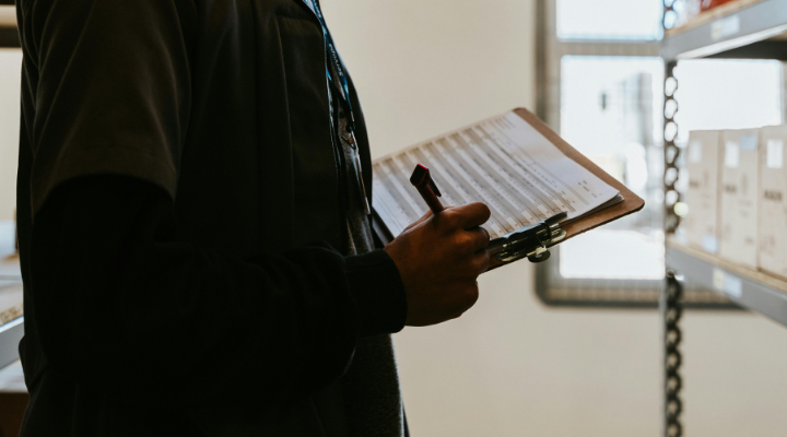 Person holding a clipboard by a shelf