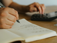Person writing in notepad and using calculator