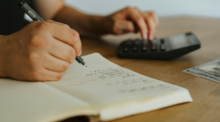 Person writing in notepad and using calculator