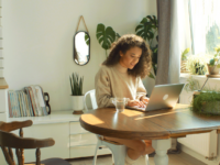 curly-haired-woman-sitting-at-dining-table-in-front-of-laptop