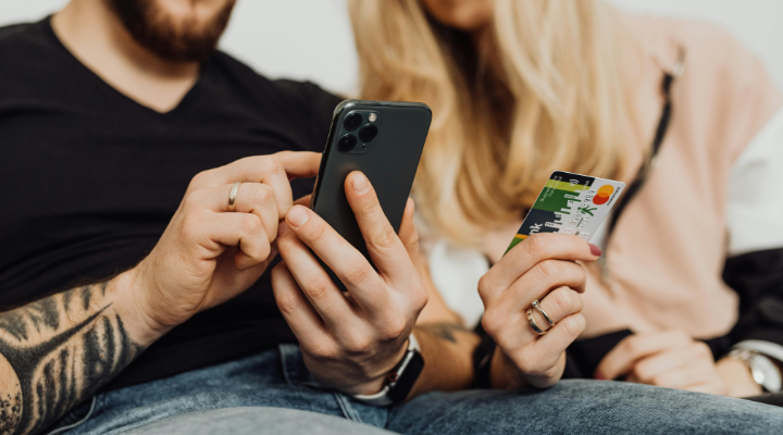 man-holding-and-tapping-iphone-sitting-next-to-woman-holding-credit-card