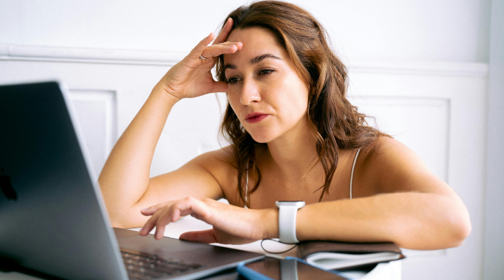 frowning-woman-with-hand-to-forehead-sitting-in-front-of-laptop
