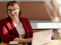 Woman in red blazer using wheelchair sitting at desk with laptop.