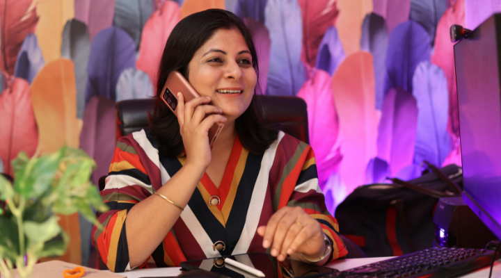 Woman wearing a colourful striped top talks on phone at desk