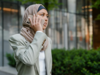 Woman wearing hijab and blazer talking on phone.