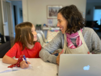 Working mother sits at table with her laptop and daughter