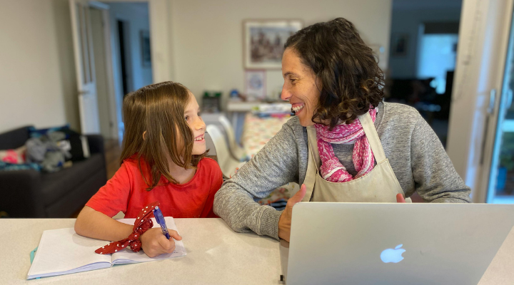 Working mother sits at table with her laptop and daughter